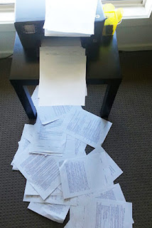 A photograph of papers spilling off the printer and across the floor.  