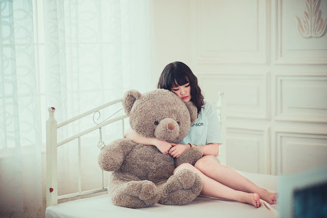 sad girl with teddy bear on bed in white room