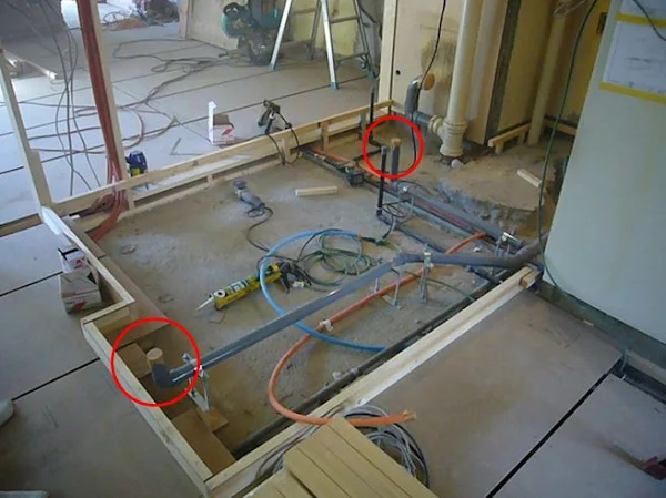 住宅建設中の床下配管の様子。給排水用の配管が床下に設置されており、赤丸で囲まれた部分には立ち上がり配管が見える。配管には給水、排水、ガスなどが含まれており、周囲には工具や資材も置かれている。