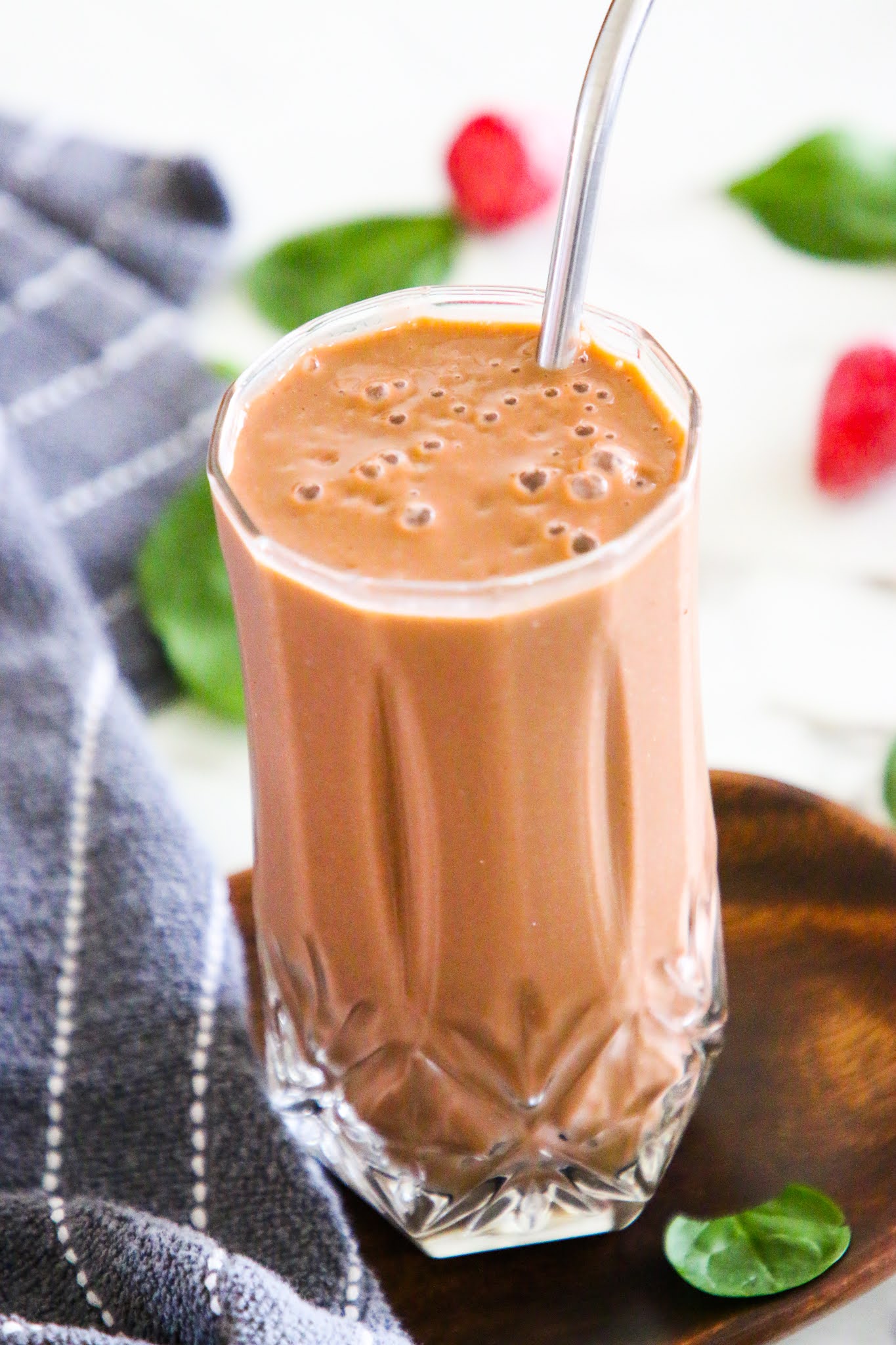 Strawberry banana spinach smoothie on a wood platter with spinach and strawberries scattered on a marble table top with a dish towel in the background.