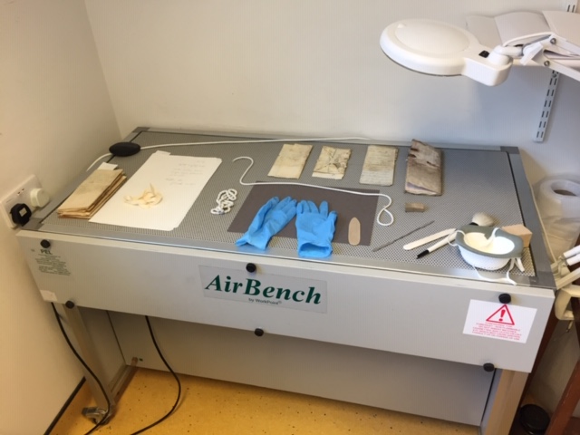 Mould documents on a perforated air bench waiting to be cleaned. Also on the table are nitrile gloves, a mask, various snake weights, brushes and spatulas.
