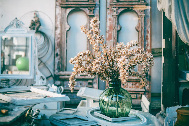 A shabby chic set up featuring flowers ina  clear blue vase and aged wardrobes in the back.