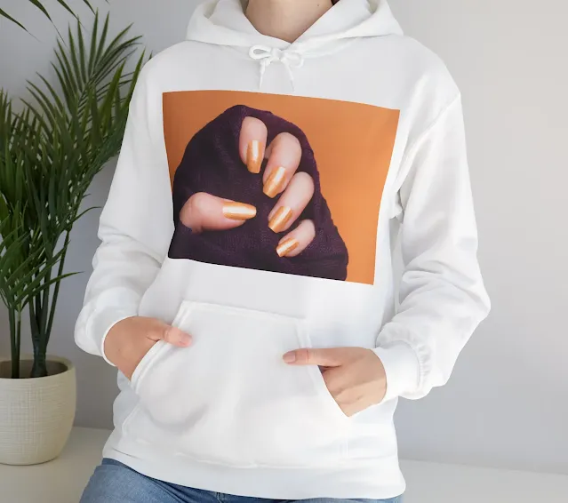A Hoodie With Female Hand with Beautiful Gold Colored Nails in Purple Clothing on Orange Background, Manicure Concept