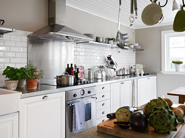 White kitchen in a Swedish cottage white subway tile backsplash stainless appliances marble counter tops white drawers and cabinets