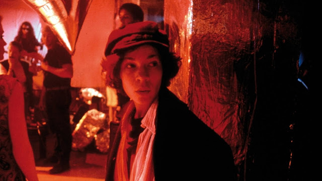 Film still from I Shot Andy Warhol. Red lighting. Valerie Solanas is at a party.