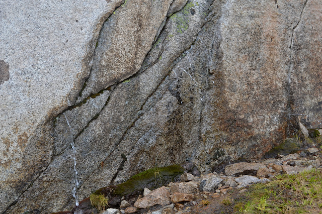 thin streams of water squirting horizontally from holes in a boulder