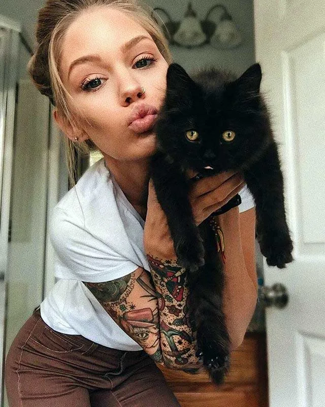 Imagen de chica joven sosteniendo un gato negro.  Ella luce tatuaje de protección