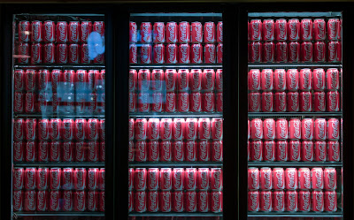 Unsplash - Ashkan Forouzani: Cans of soda displayed in refrigerated cases