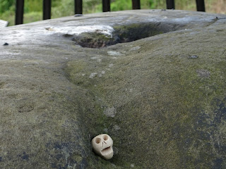 A photo of a small, ceramic skull (Skulferatu 74) lying in a hollow in the Beheading Stone on Mote Hill in Stirling. Photograph by Kevin Nosferatu for the Skulferatu Project.