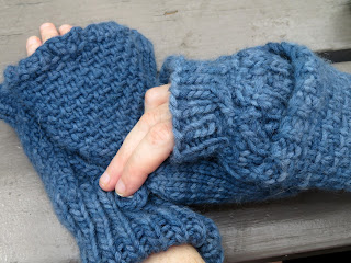 person wearing a pair of flip-top convertible mittens.  They are unbuttoning the left-hand mitten from the back of the hand.