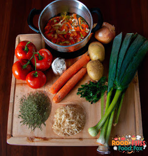 Image of all the ingredients needed to make the soup. The vegetables and herbs are organized in a wooden board, and the can of diced tomatoes and vegetable broth are next to it.
