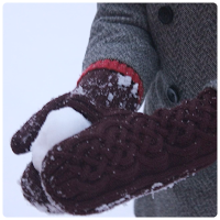 Close up of a pair of burgundy cabled mittens making a snowball.