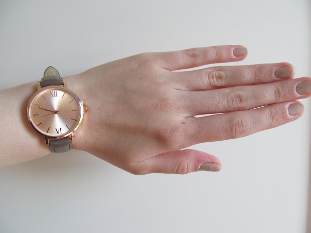 Rose gold watch on wrist with mauve nail polish matching mauve/khaki strap of watch