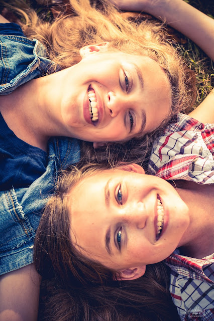 two sisters laying with heads side by side in the grass