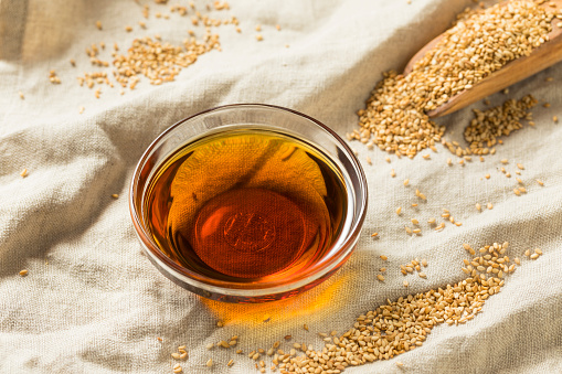 Sesame oil in a bowl and some sesame seeds on floor