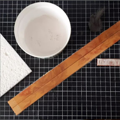 Flat lay of a cutting mat showing 2 strips of bamboo table runner with, around it, a container of cleaning paste and a sponge, a piece of steel wool and a sanding stick