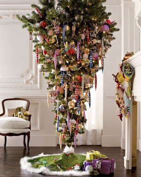 Beautifully decorated upside-down Christmas tree standing between a white chair and a fireplace in a white paneled room