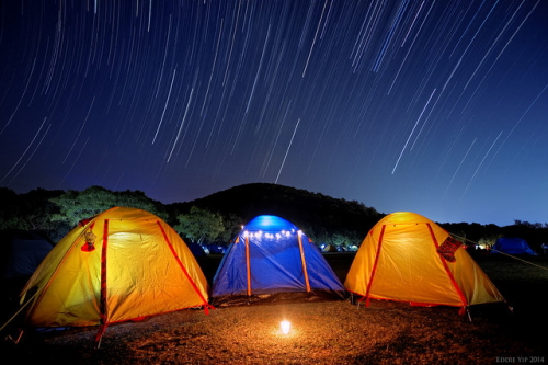 夜のキャンプ場に3つの明かりの灯ったテント、夜空には流星群。