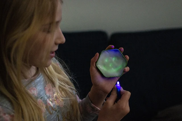 A girl in a dark room holding glow in the dark putty with a face glowing on it and holding a uv light