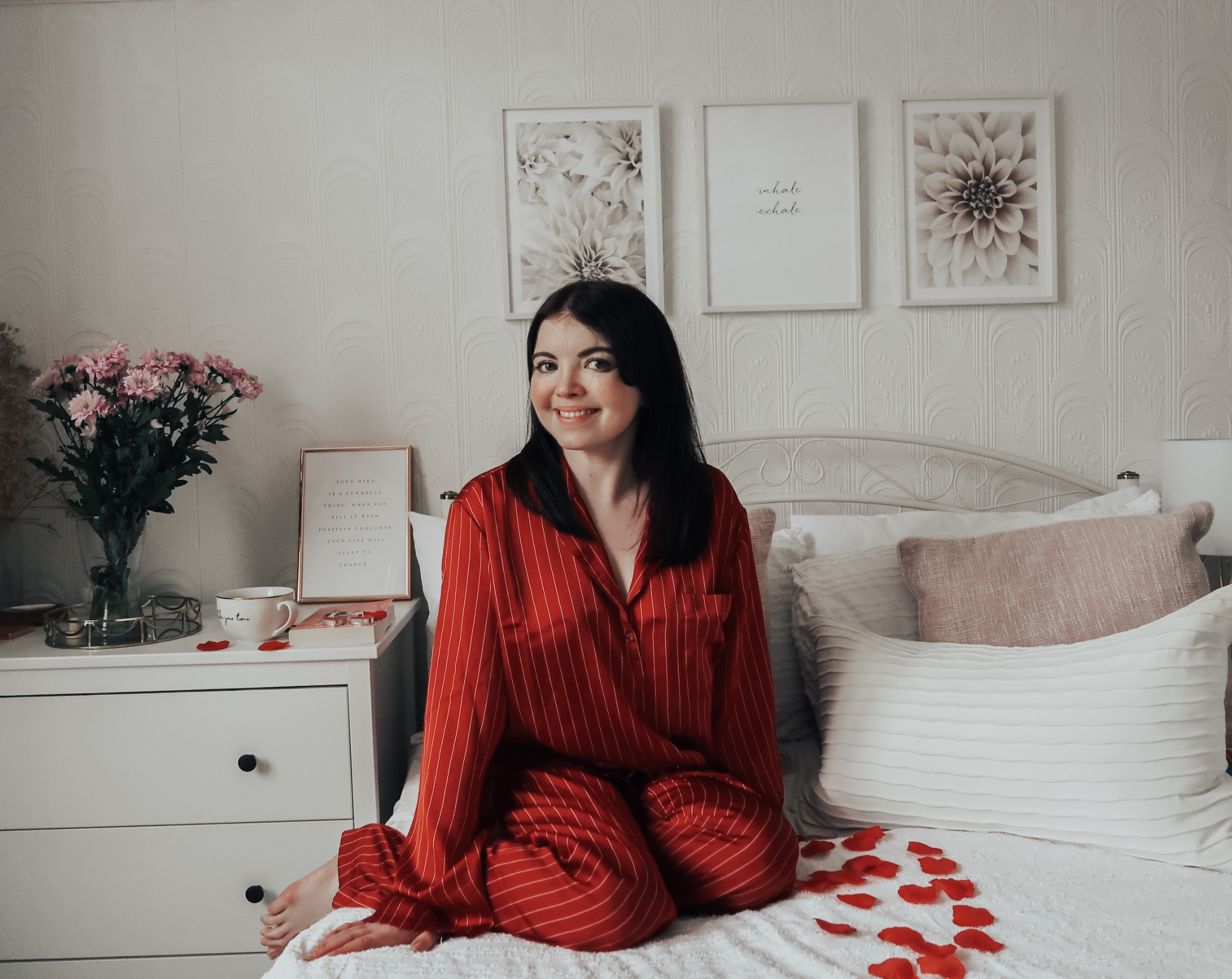 A woman sat on a bed in red pyjamas.