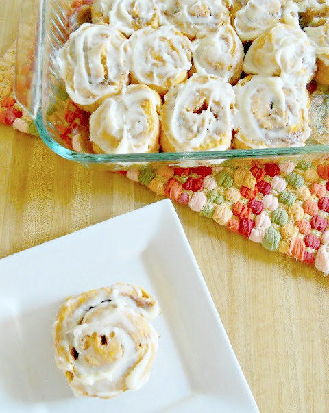 Pumpkin cinnamon rolls in a glass baking dish with one on a white plate.