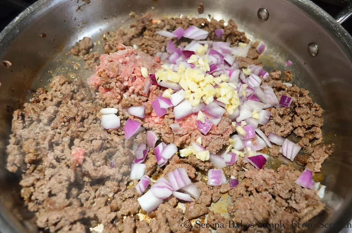 A down shot of browned ground beef, onion, and garlic in a stainless steel pan.