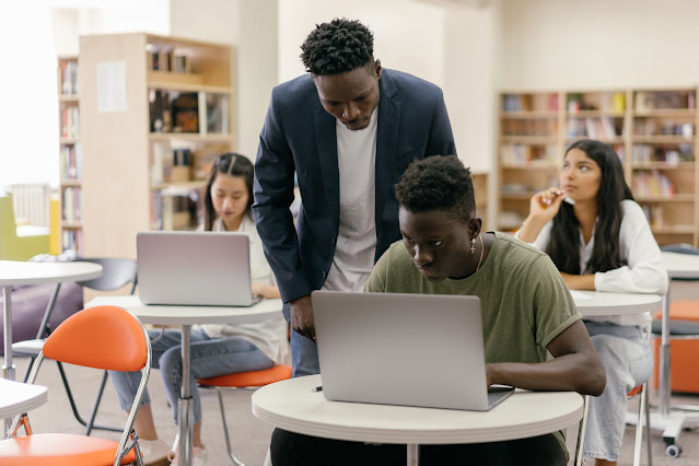 a black teacher male teaching a black male student using laptop in school