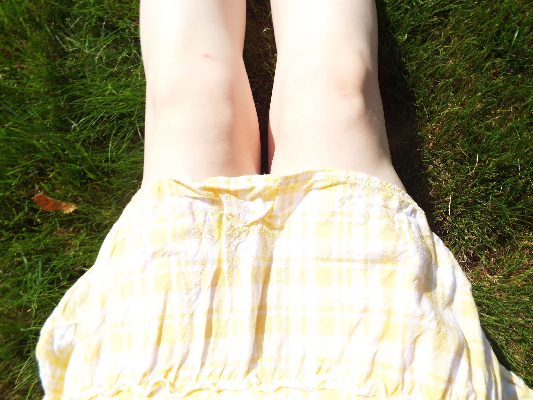 Sitting on the grass on a bright, sunny day, with legs stretched in front and my yellow gingham dress resting over my legs, just above my knees.