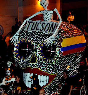 A giant bedazzled skull with a skeleton on top being pulled by costumed people. All Soul's Procession, Tucson AZ 