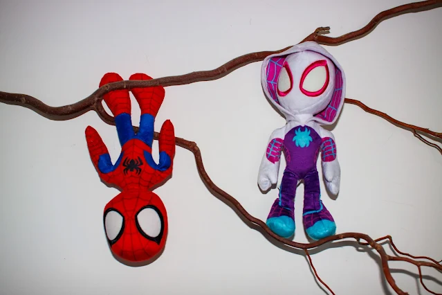 Spiderman hanging upside down from a branch with Ghost Spider near by