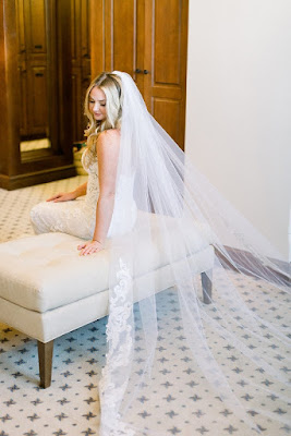 bride sitting on beige bench with long veil behind her
