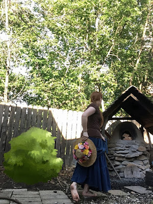 A redheaded white woman walking away from the camera, toward a small cob-and-stone bread oven under an A-frame shake shingle roof, with an obviously photoshopped green "bush" to her left and backlit by the intense sunlight on the weathered wooden fence in front of her. Her hair is braided with a long tail, and falls over her right shoulder. She'sfacing the oven, with her right arm canted behind her holding a large-brimmed sunhat with a dense crown of bright-yellow, peach, coral, pale-pink, and purple flowers and her left hand just visible holding the fabric ties of the hat. She's wearing a brown shirt and long denim skirt, and silver bracelets on each wrist. Her feet are bare, and thedirty cole of her left foot shows as she takes a step.The medium-blue fabric ties falling from the inside of the hat blend into her skirt almost perfectly. Trees washed in brilliant sunlight fill the background, almost blocking out the sky.