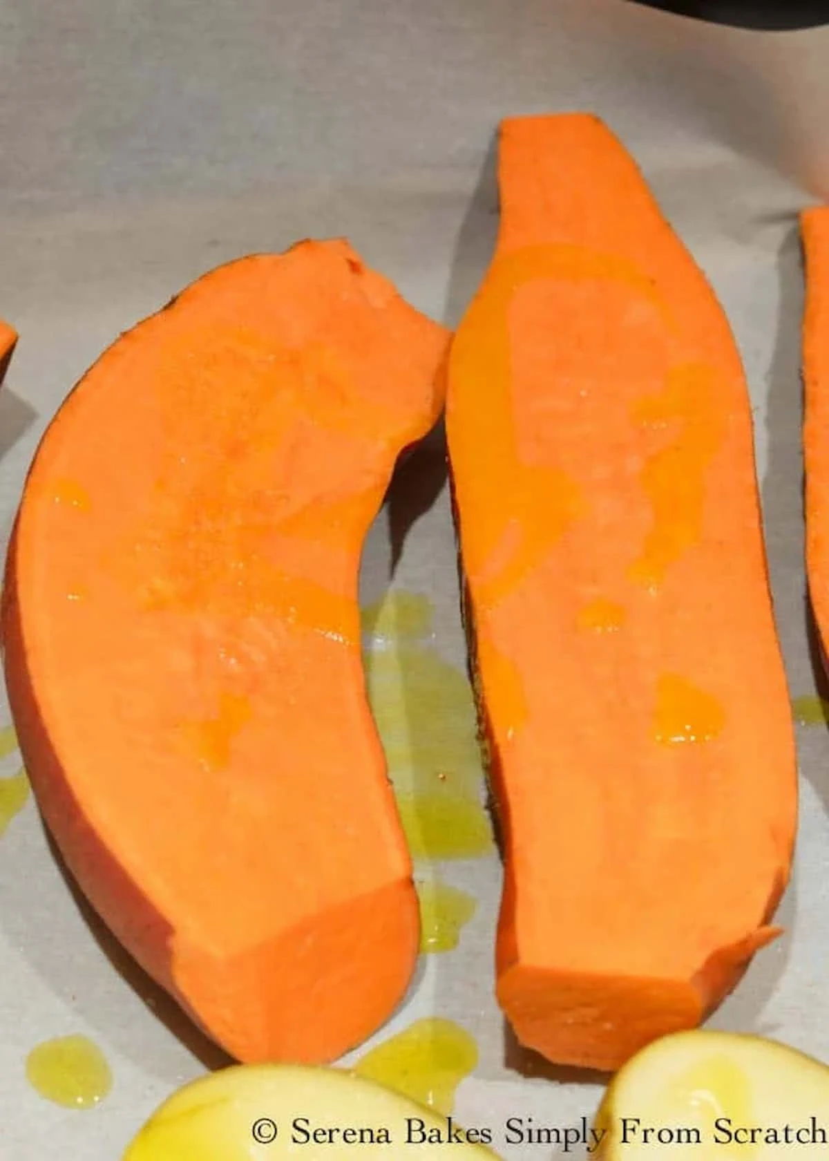 Sweet Potatoes sliced in half and drizzled with olive oil on a parchment lined baking sheet.