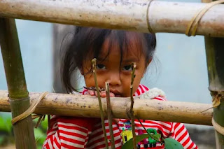 An image of a child girl behind he fence in red cloth- sad girl dp