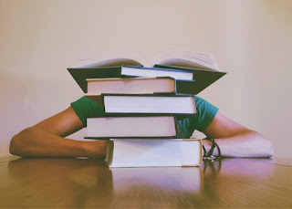 Student hidden, possibly sleeping, behind stack of books.