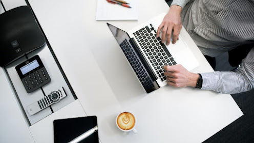 A marketer at work on a computer with a smartphone and a creamy cup of coffee on the table.