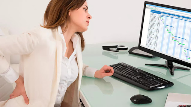 Aliviar el lumbago en casa: mujer trabajando frente a un ordenador y tocando la parte lumbar por sentir dolor