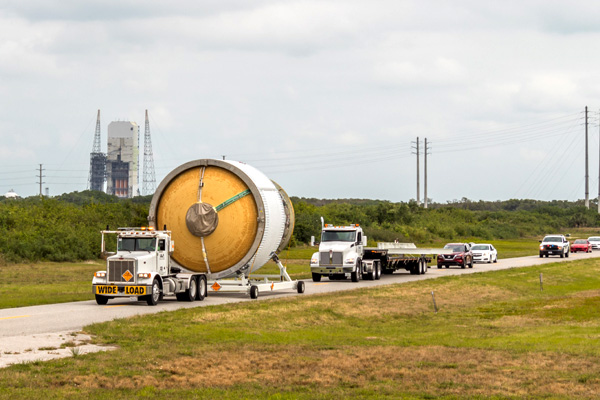 With a Delta IV Heavy rocket visible in the background at Cape Canaveral Space Force Station's SLC-37B in Florida, the Interim Cryogenic Propulsion Stage (ICPS) that will fly on NASA's Artemis 2 mission is transported to United Launch Alliance's (ULA) Delta Operations Center.