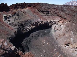 A photo looking at the stratigraphy of the Ngauruhoe scoria cone at the summit of the volcano. There are layers of rock including red scoria, grey ash, and grey spatter deposits.