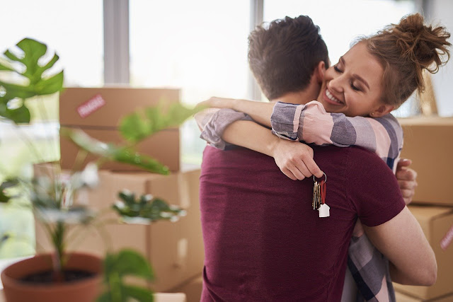 Couple hugging in front of cardboard boxes with house keys in hand