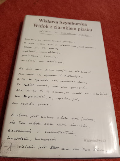 Na czerwonej tkaninie zaprezentowano tomik poezji Wisławy Szymborskiej zatytułowany Widok z ziarenkiem piasku.