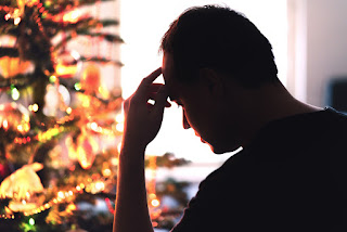 Silhouette of a person holding their head with a lighted Christmas tree in the background.