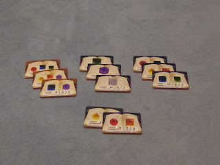 Three stacks of three and one stack of two cards. Each card has one or more colour (or blank sword tiles icons) and a rule for how they are scored on a background that looks like an open book.