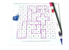 na zdjęciu plansza do gry z zakreślonymi już polami, po lewej stronie leży niebieska kostka do gry a po prawej różowy pisak