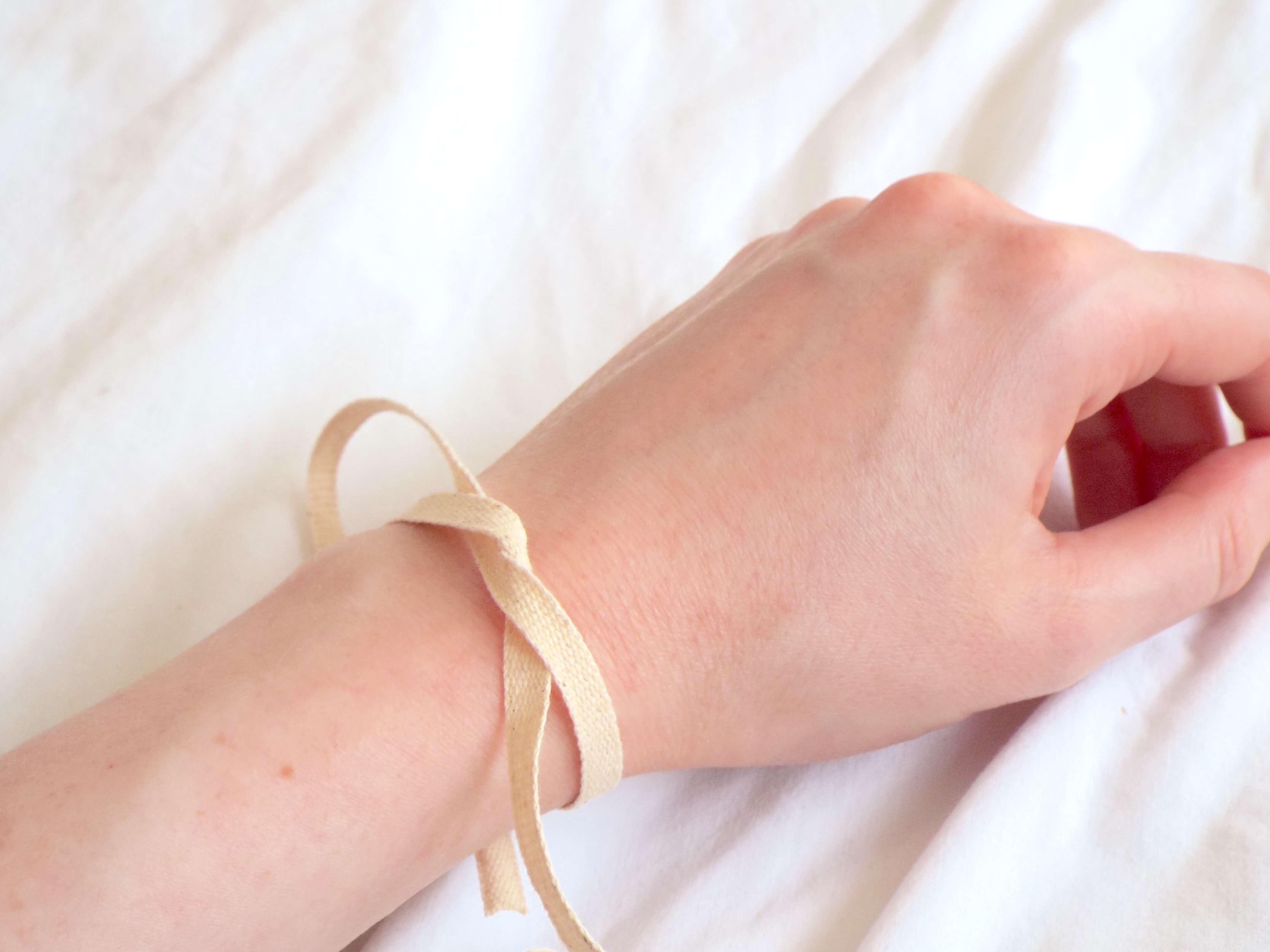 Me demonstrating the cream cotton ribbon that came holding the protective card candle wrap together as a simple bracelet tied in a single not around wrist.