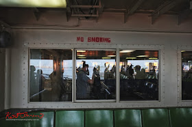 Seating on an open deck section of a Staten Island Ferry, reflections and silhouettes of commuters. No Smoking Sign.  Travel photography by Kent Johnson.