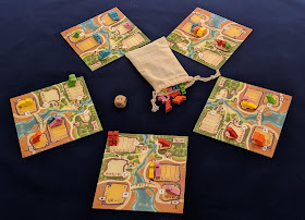 The five player boards, with some of the dinosaur meeples placed on them, and the bag of dinosaur meeples with the large wooden die.