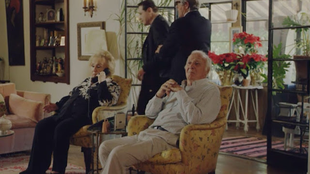 A very old Doris Roberts and Robert Loggia sit in chairs in a nursing home.