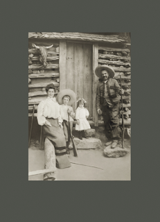 Morris, Molly, Henry and Pearl Blatt in Mineral Wells Texas. They pose in front of a log cabin. Henry is holding a rifle.