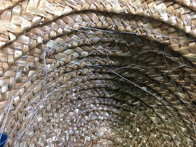The inside of a straw hat crown, with random crisscrossed white threads stitched across it, mostly sticking close to the walls, but occasionally leaping across sections.